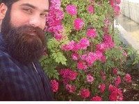 سلفی علی زند وکیلی با یک درختچه گل زیبا در کنار مصرعی از حضرت حافظ