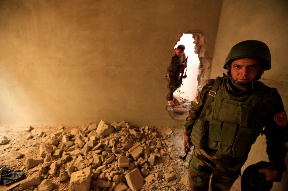 A member of Peshmerga forces walks through a hole in the wall in the town of Bashiqa, east of Mosul